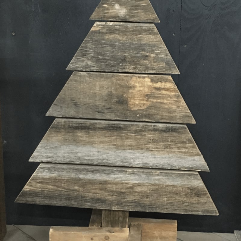 A wooden Christmas tree made of stacked planks stands against a dark black wall.