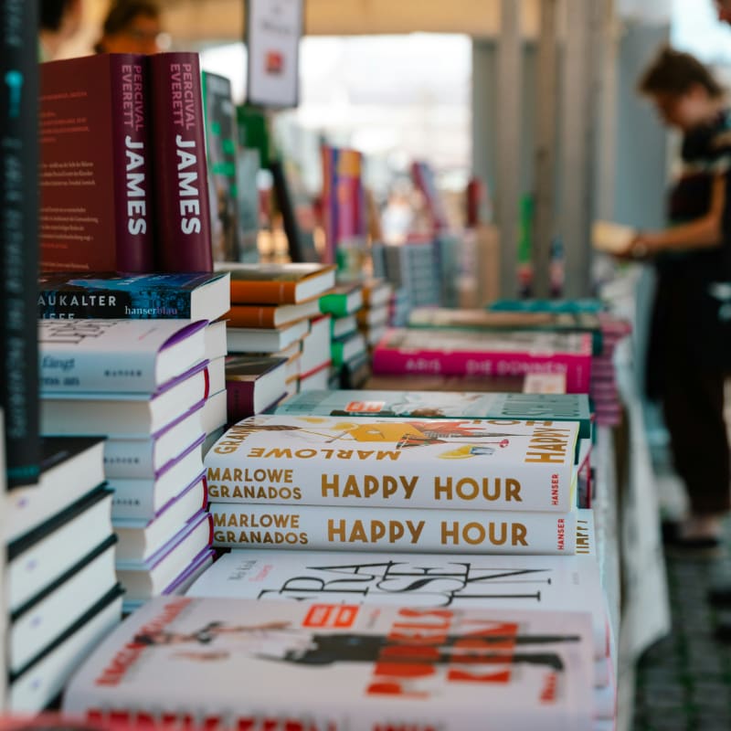 A number of books on a table with people in the background