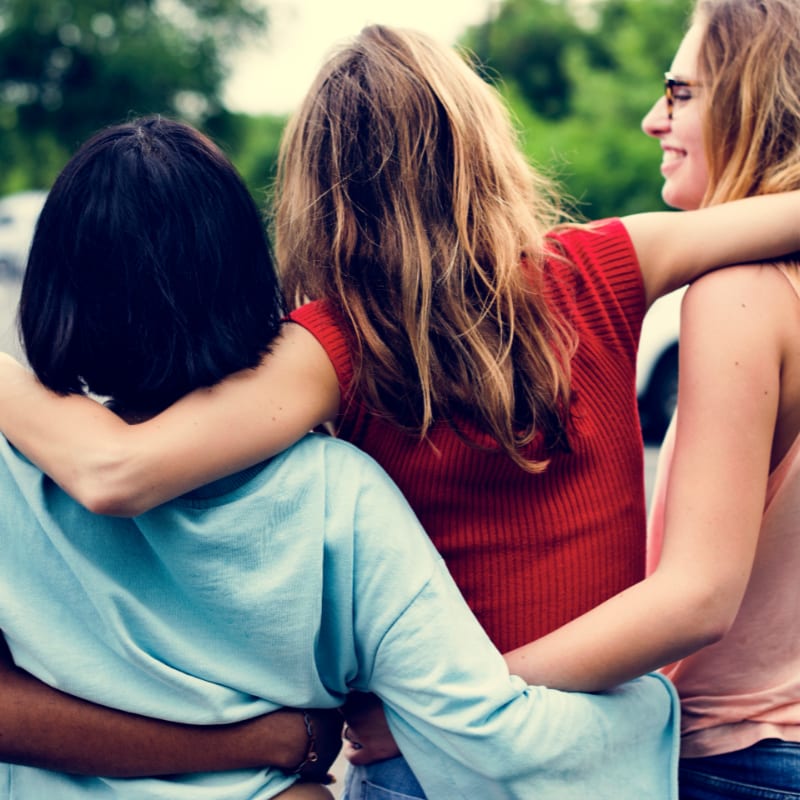 Three friends with arms around each other stand in front of a blurred green background.