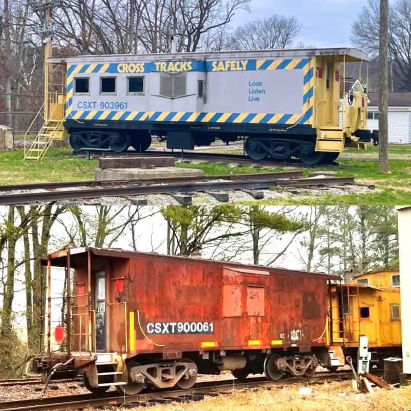 Two railway cars, one blue and yellow and one rusty red, sit on tracks against a backdrop of bare trees.