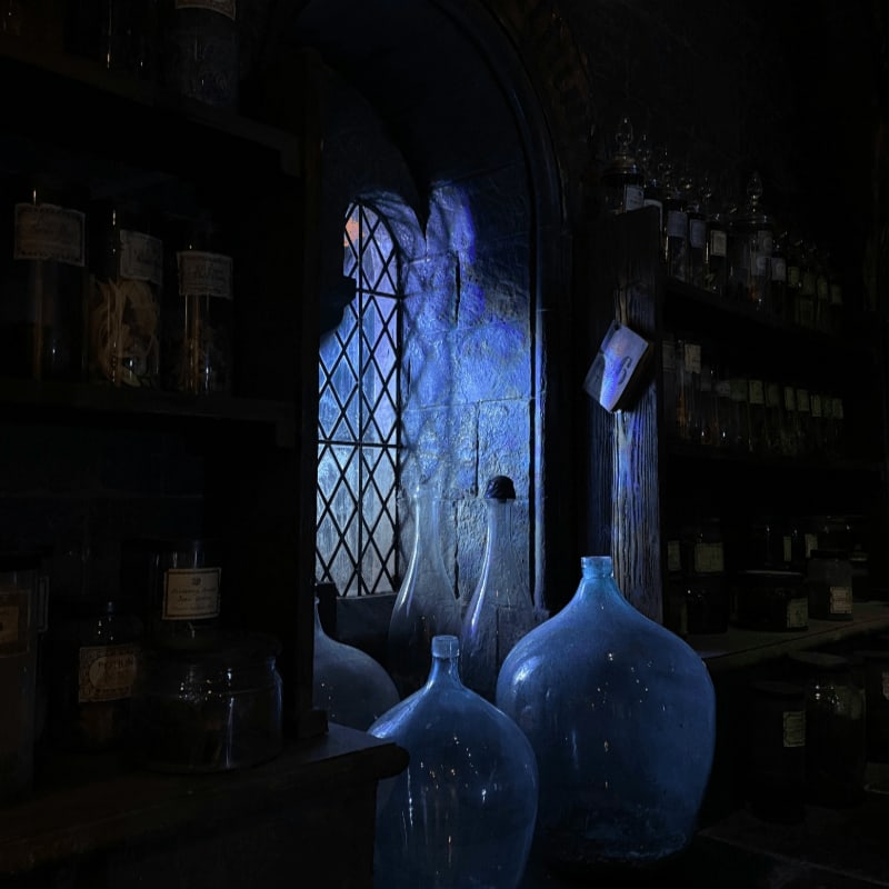 Glass bottles on shelves and a large blue bottle near a stone window