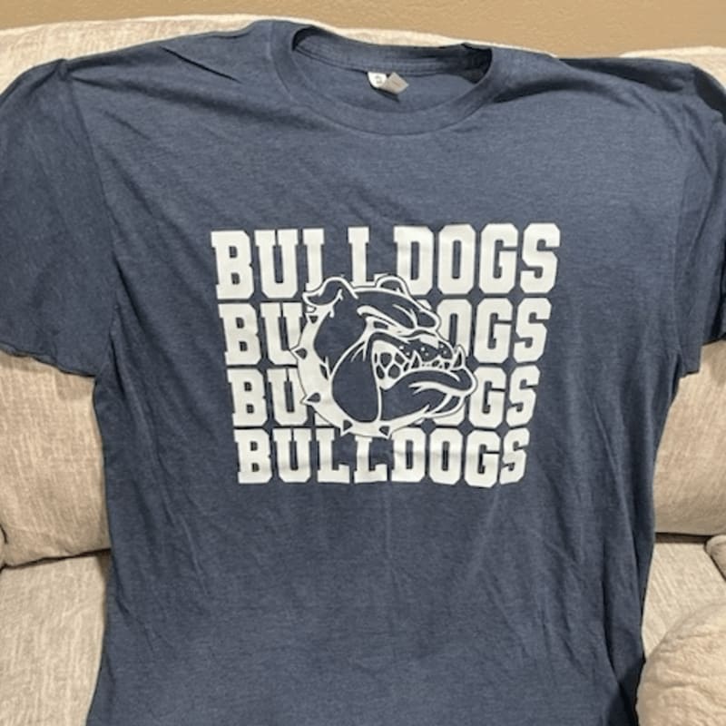 A blue t-shirt with a white bulldog logo and text rests on a beige couch.