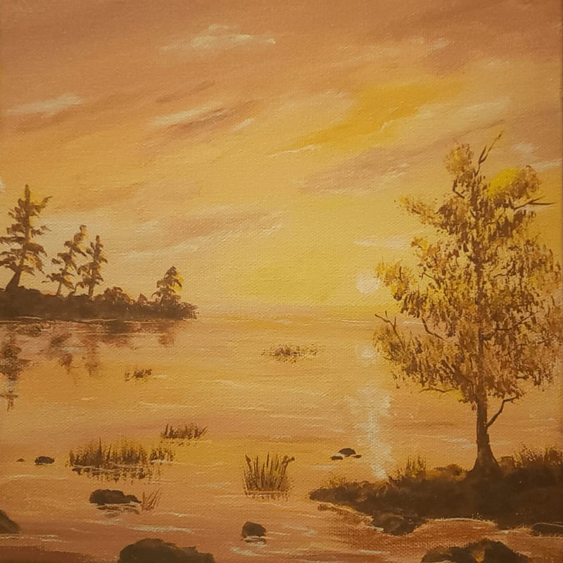 A solitary tree and rocky shoreline stand in the foreground of a golden sunset reflecting over a calm body of water.