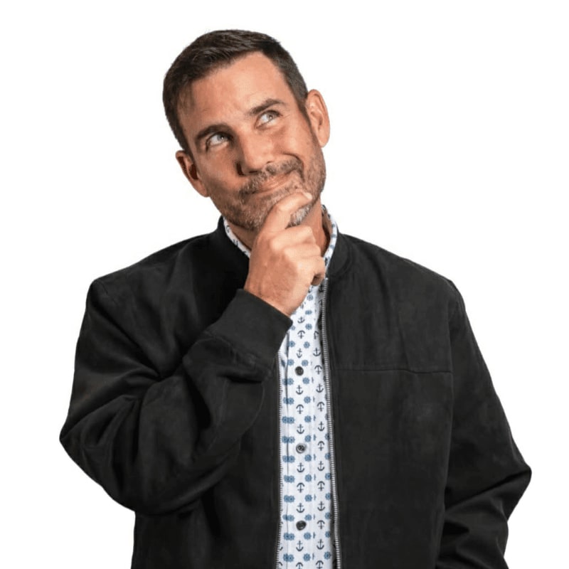 A thoughtful man in a black jacket and anchor-print shirt stands against a plain white background.