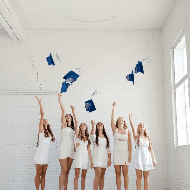 a group of young women in graduation gowns throwing their caps in the air