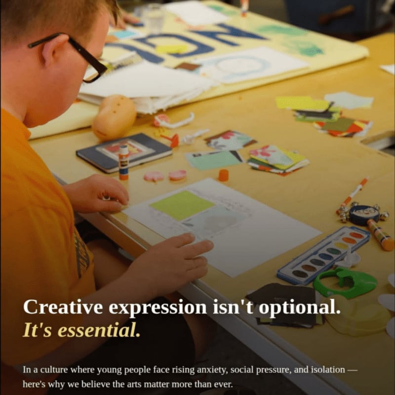 A young boy in a yellow shirt works on an art project at a table filled with supplies, with a blurred classroom setting in the background.