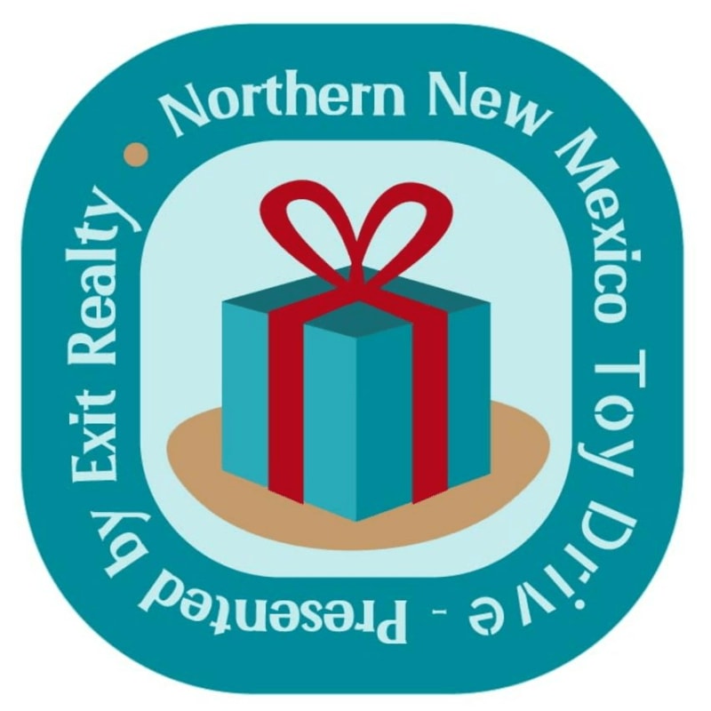 A blue gift box with a red ribbon sits on a tan surface, centered within a light blue frame and surrounded by a teal circular border containing the text "Northern New Mexico Toy Drive - Presented by Exit Realty".