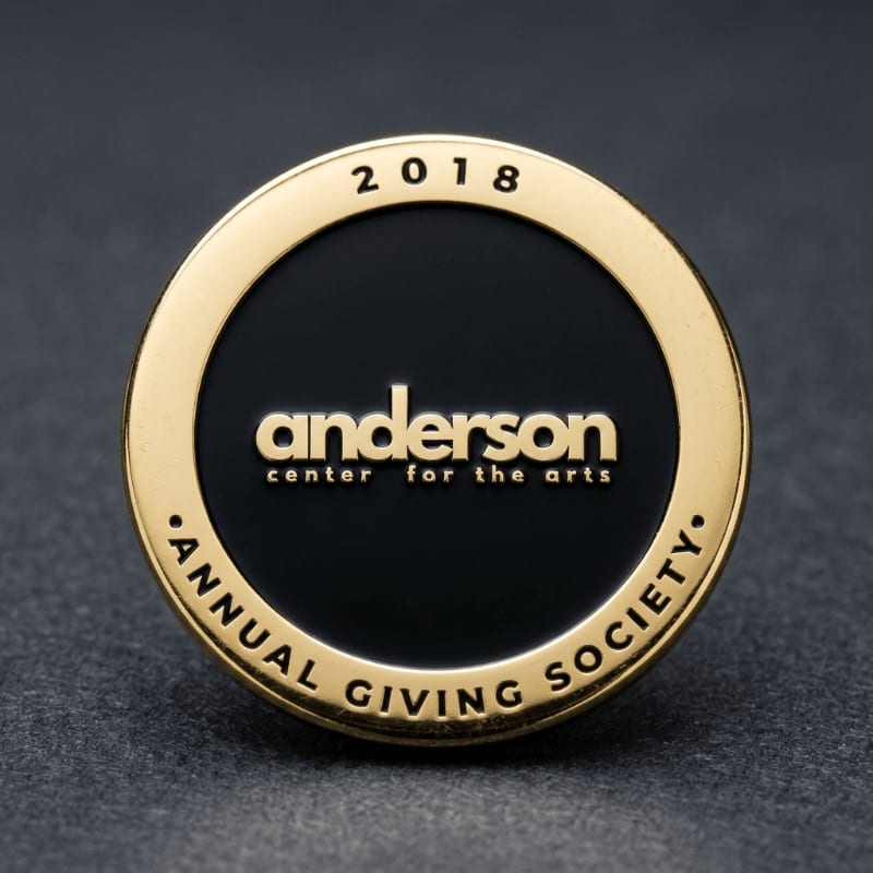 A gold and black commemorative coin for the Anderson Center for the Arts rests on a dark, textured surface.