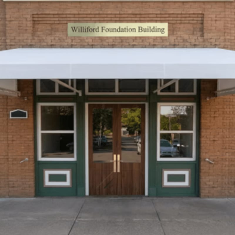 A white awning hangs over the wooden double doors and green-trimmed windows of the brick Williford Foundation Building.