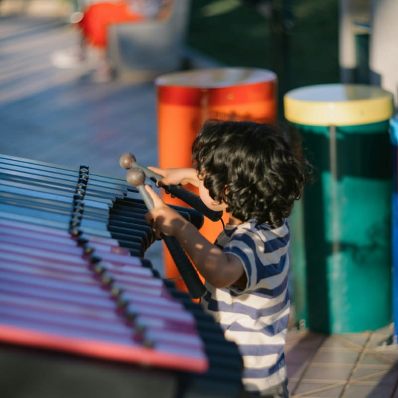 Child playing xylophone outdoors with colorful drums behind