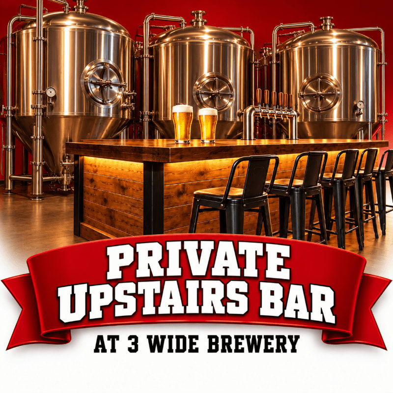 A wooden bar with stools and two glasses of beer sits in the foreground, set against a background of large stainless steel brewing vats and a red wall.