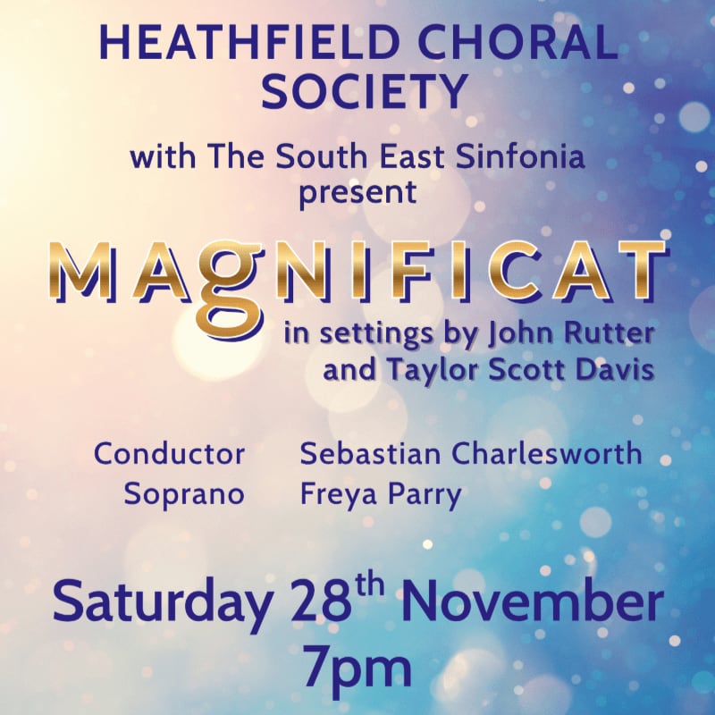 Blue and gold text announcing a Magnificat concert by the Heathfield Choral Society is set against a soft, bokeh-style background of blue and white light.