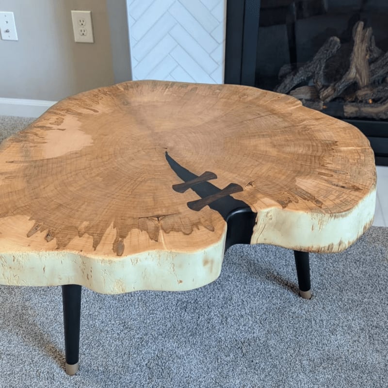 A live-edge wooden coffee table with a black resin inlay sits on a grey carpet in front of a fireplace and a white herringbone wall.