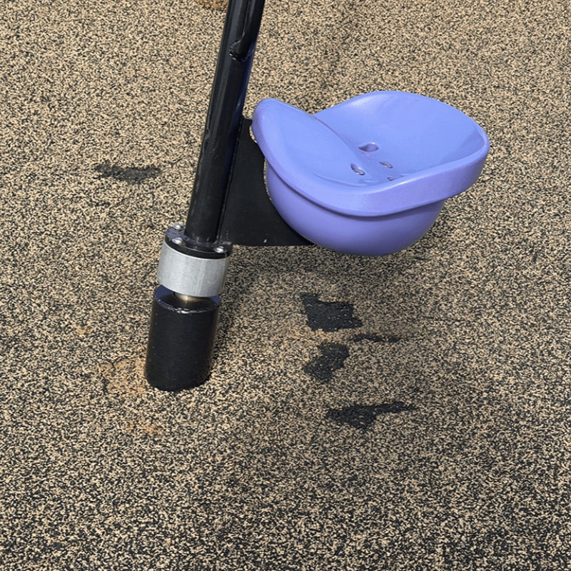 A purple plastic cup holder is attached to a black pole standing on a textured brown ground.