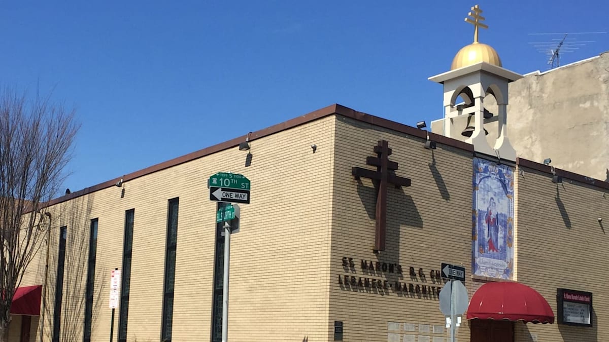A tan brick church with a large cross and a golden dome stands under a clear blue sky.