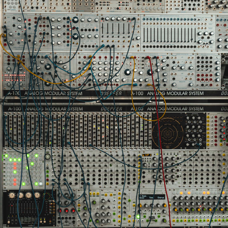 Modular synthesizer rack with many knobs and tangled patch cables
