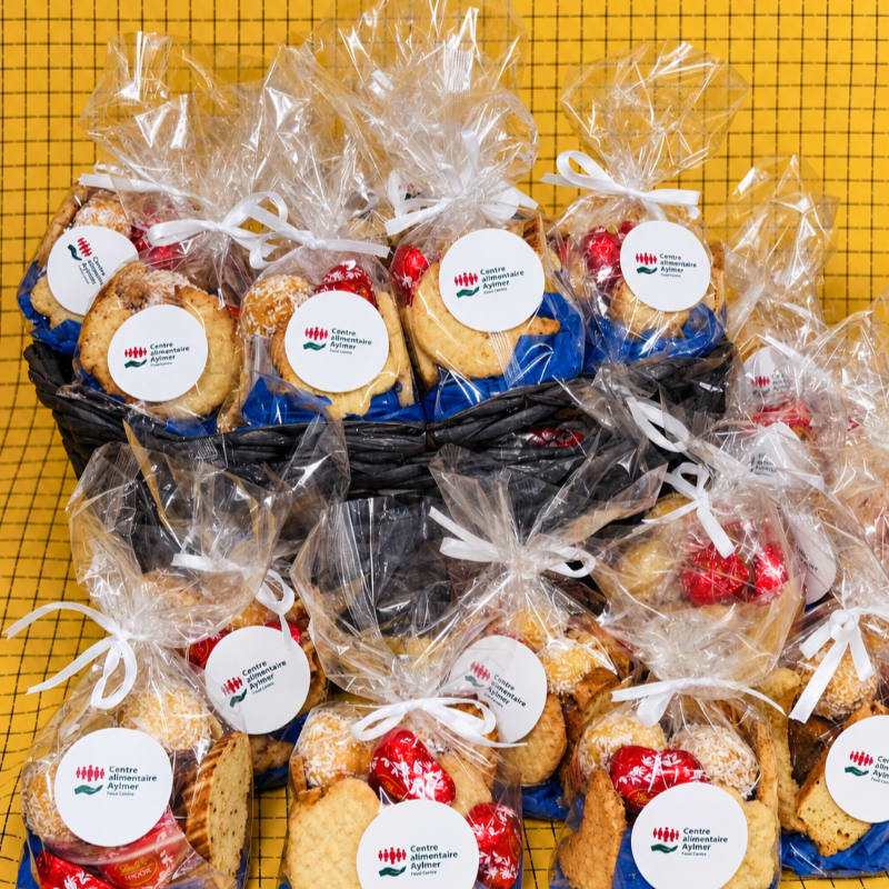 Clear plastic bags filled with baked goods and red candies sit in a black basket against a yellow grid background.