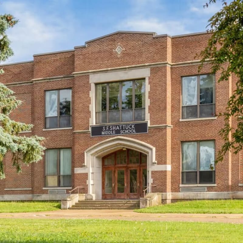 A brick middle school building stands behind a green grassy lawn under a blue sky.