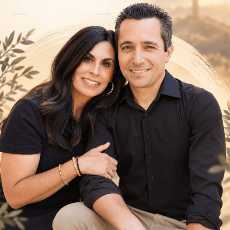 A smiling couple in black shirts poses together against a soft, golden-toned background with subtle leaf accents.