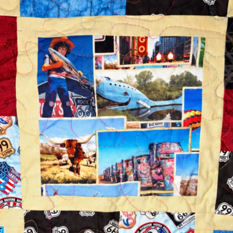A colorful quilt square features a collage of Route 66-themed images, including a long-horn cow and a blue whale, surrounded by a yellow fabric border and patterned quilt pieces.