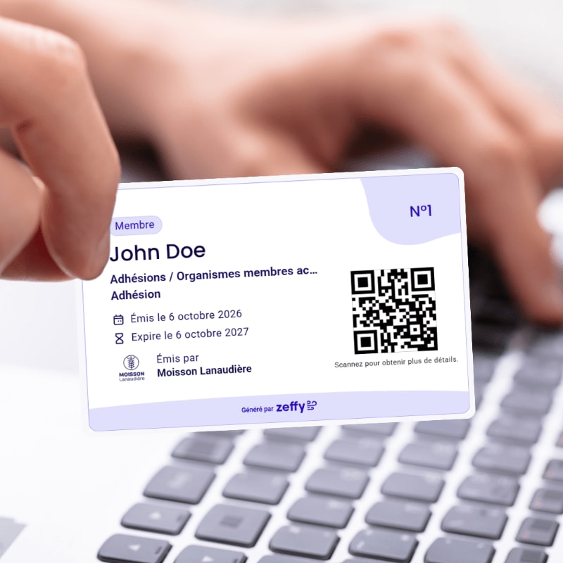 A hand holds a white membership card for John Doe over a blurred laptop keyboard and background.