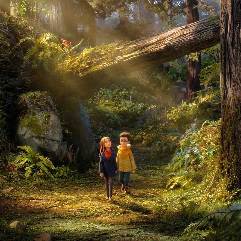 Two young children walk along a sun-dappled forest path beneath a massive, moss-covered fallen log.