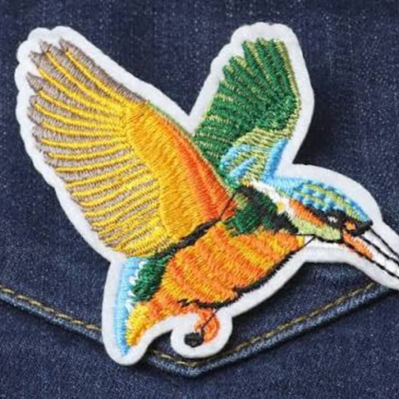 A colorful embroidered bird patch is placed on a dark blue denim fabric background.