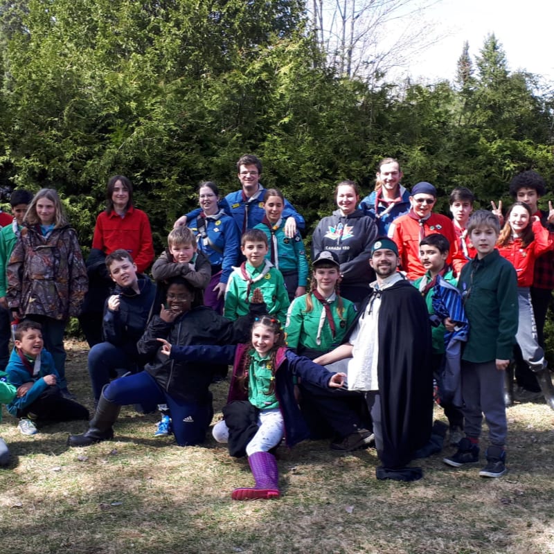 A group of people in outdoor clothing pose for a photo in front of a dense forest.