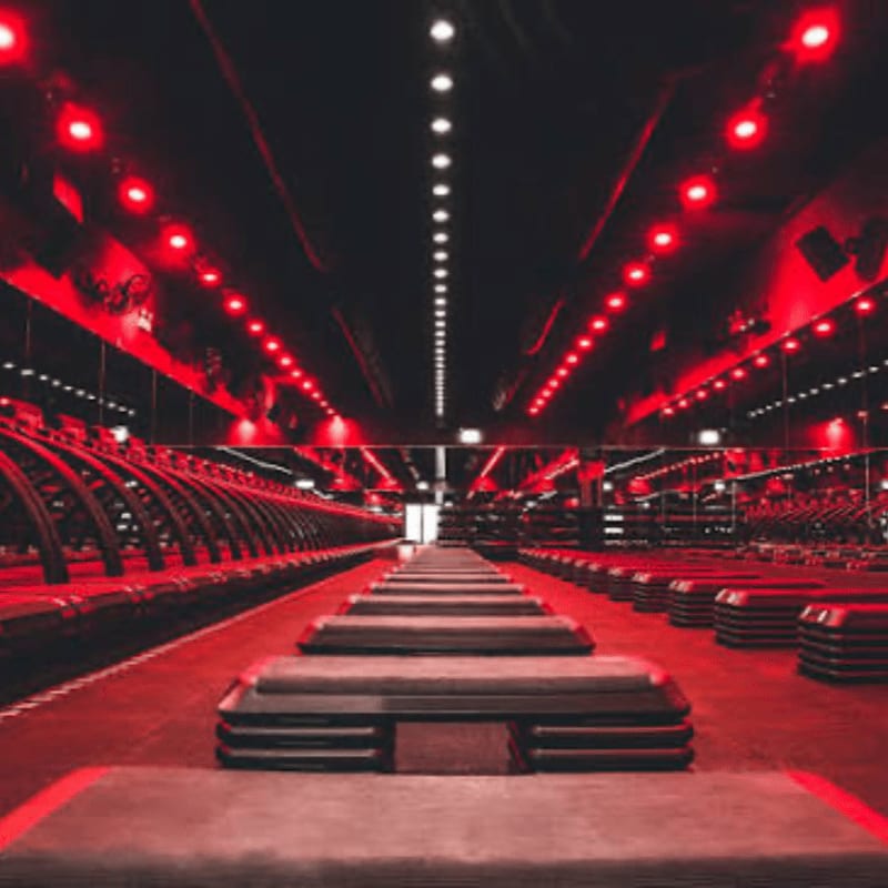 Rows of aerobic step platforms lead into a dark gym illuminated by red ceiling lights and mirrored walls.