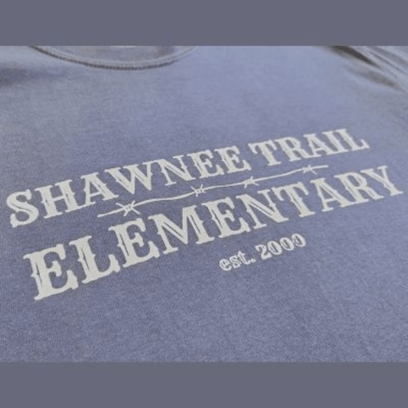 White text reading "SHAWNEE TRAIL ELEMENTARY est. 2000" is printed across the chest of a light blue t-shirt.