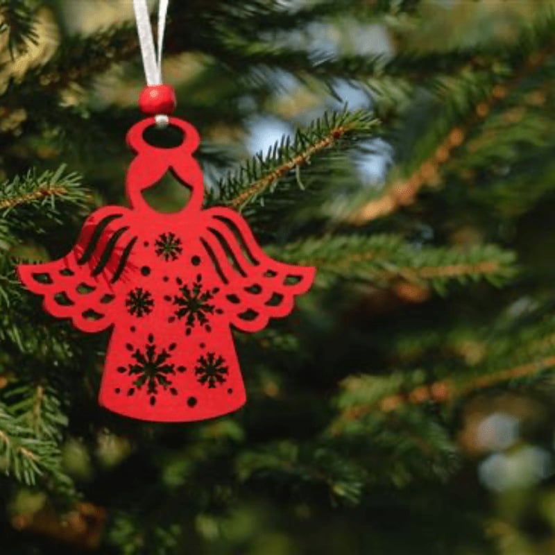 A red angel ornament with snowflake cutouts hangs from a green evergreen tree branch.