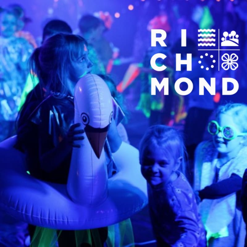 Children play in a blue-lit room with a girl holding a white swan float in the foreground and a "RICHMOND" logo overlaid on the background.