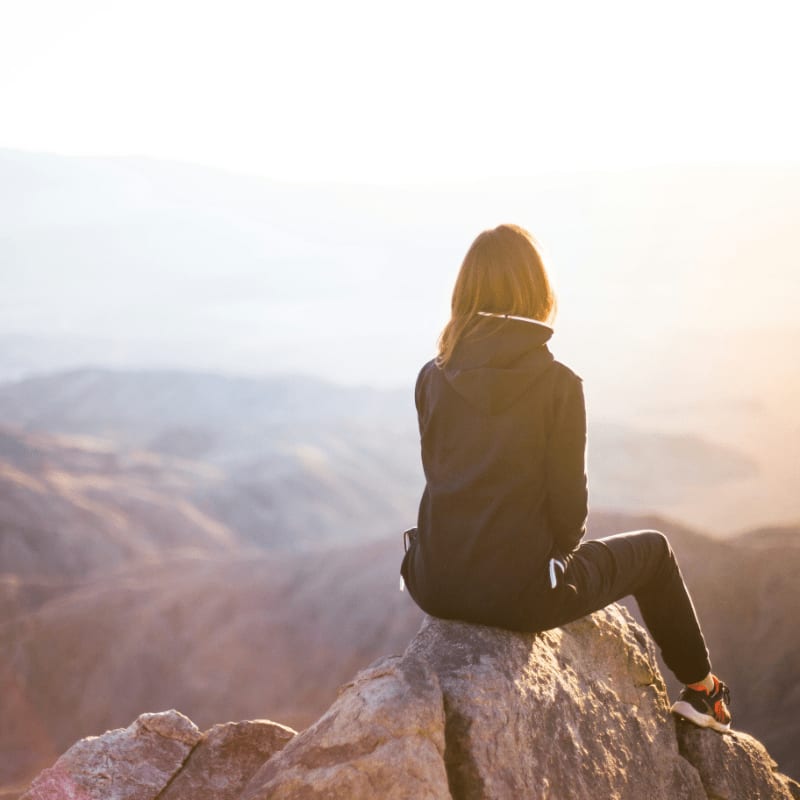 person sitting on top of gray rock overlooking mountain during daytime
