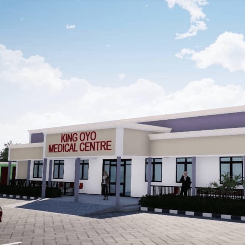 A modern medical center building with red signage stands in the foreground under a bright, cloudy blue sky.