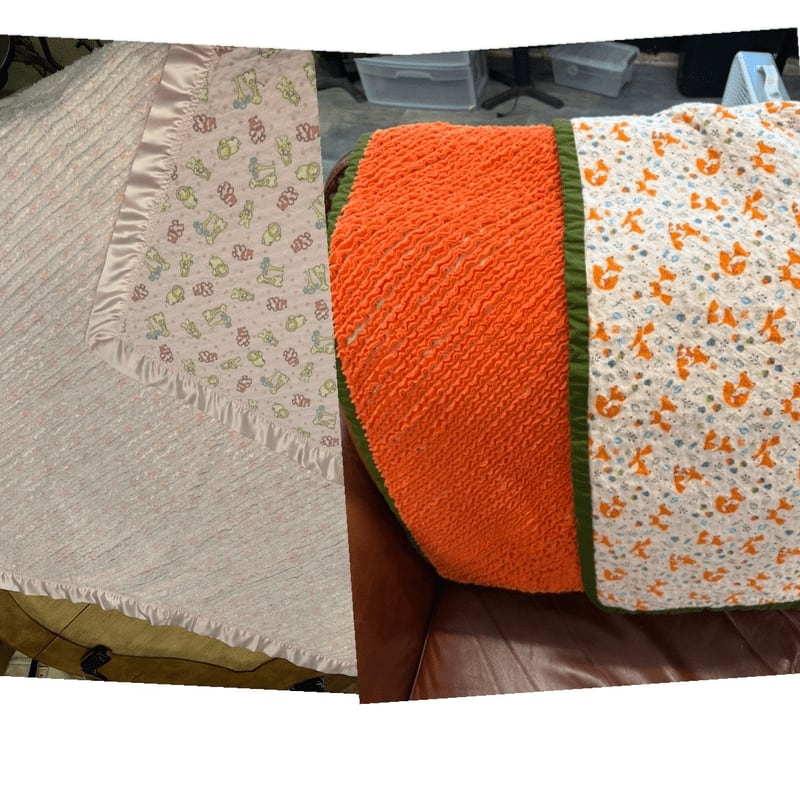 Two patterned baby blankets lie on a brown leather surface with plastic storage bins in the background.