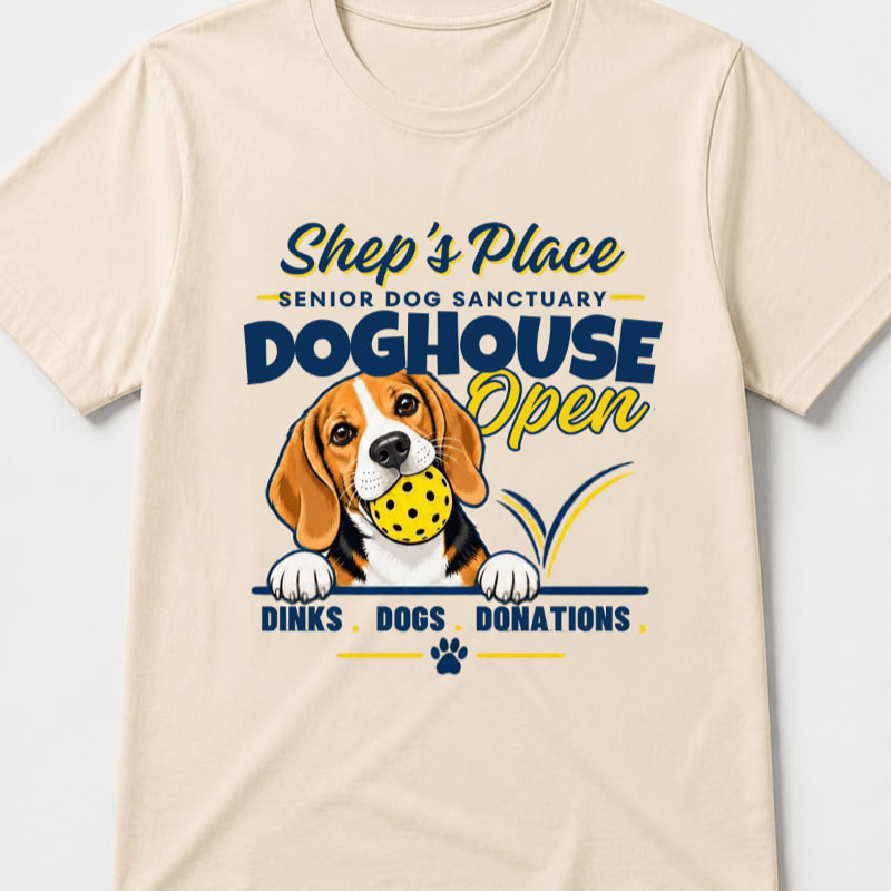 A beagle holding a yellow ball in its mouth is printed on the front of a cream-colored t-shirt.