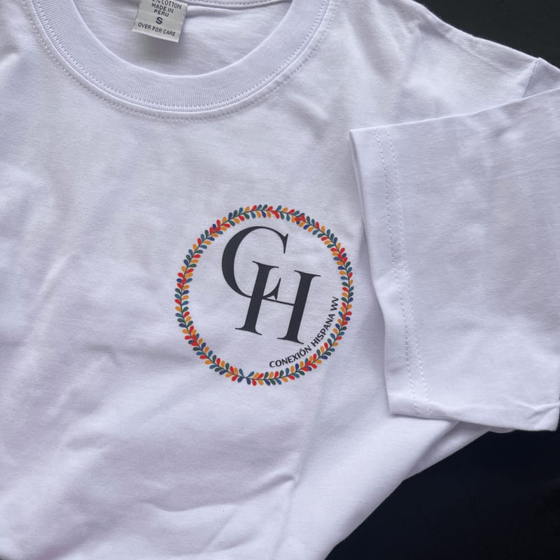 A white t-shirt featuring a circular logo with the letters "CH" and a colorful wreath is laid against a dark background.