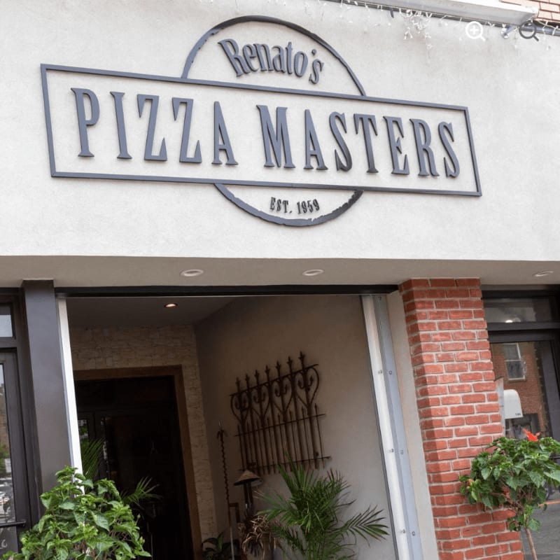 A "Renato's Pizza Masters" sign hangs on a white wall above an open storefront featuring a brick pillar and green plants.
