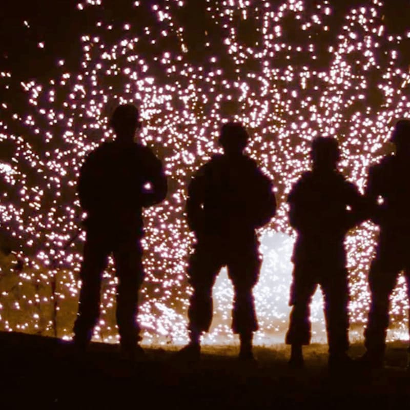 Four silhouetted figures stand in the foreground against a background of shimmering, white sparkling lights.
