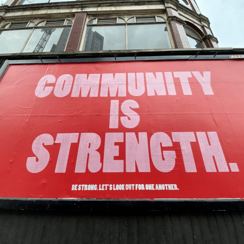 A large red billboard with white text reading COMMUNITY IS STRENGTH on a building