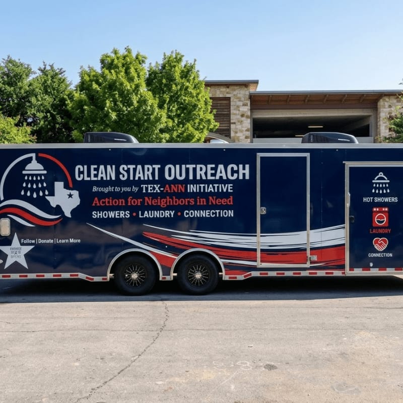 A blue "Clean Start Outreach" mobile shower and laundry trailer is parked on a concrete lot in front of green trees and a stone building.