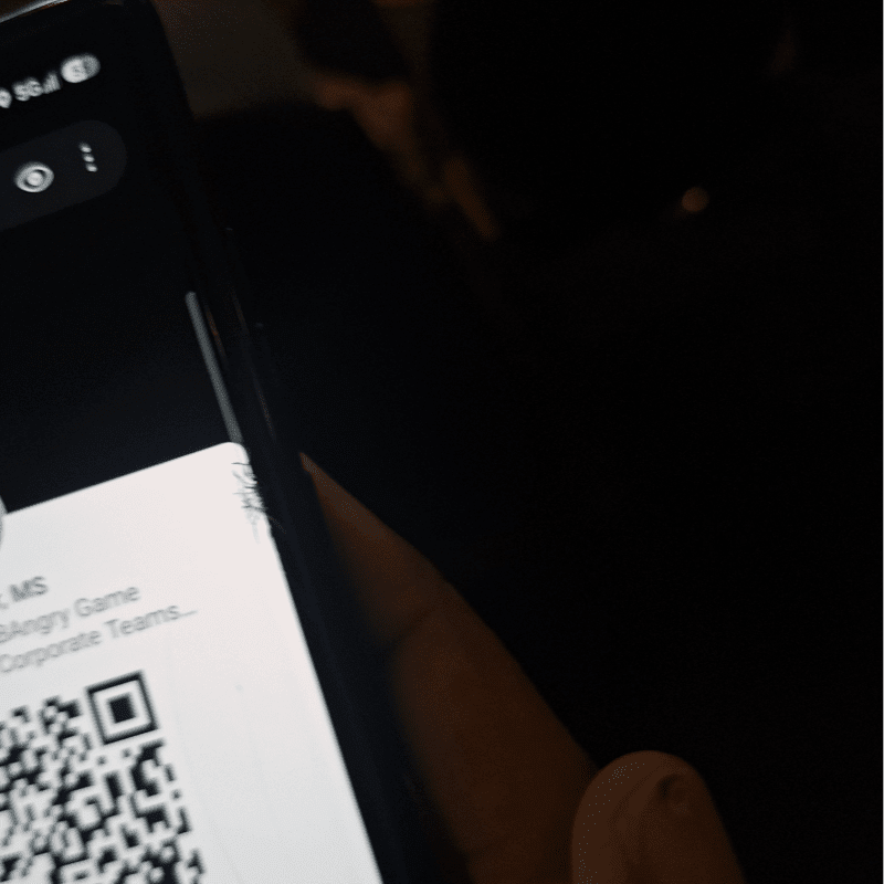 A close-up of a smartphone screen displaying a QR code is held against a dark, blurred background.