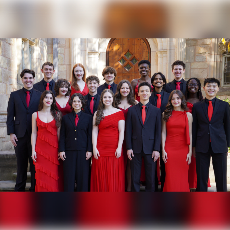 A group of young people dressed in formal red and black attire pose for a photo in front of a stone building with a wooden door.