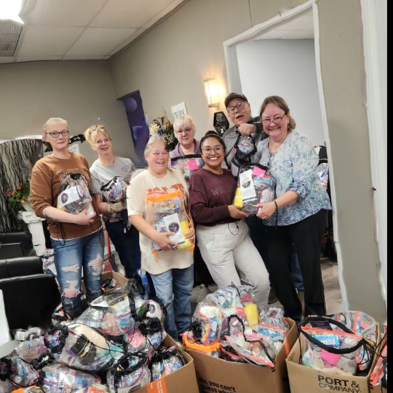 A group of smiling people stand behind boxes filled with gift bags inside a neutral-toned room.