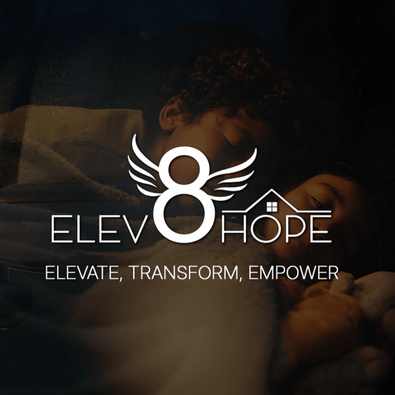 A white "Elev8 Hope" logo with wings and a house icon sits in the foreground over a dark, blurred background of two sleeping children.