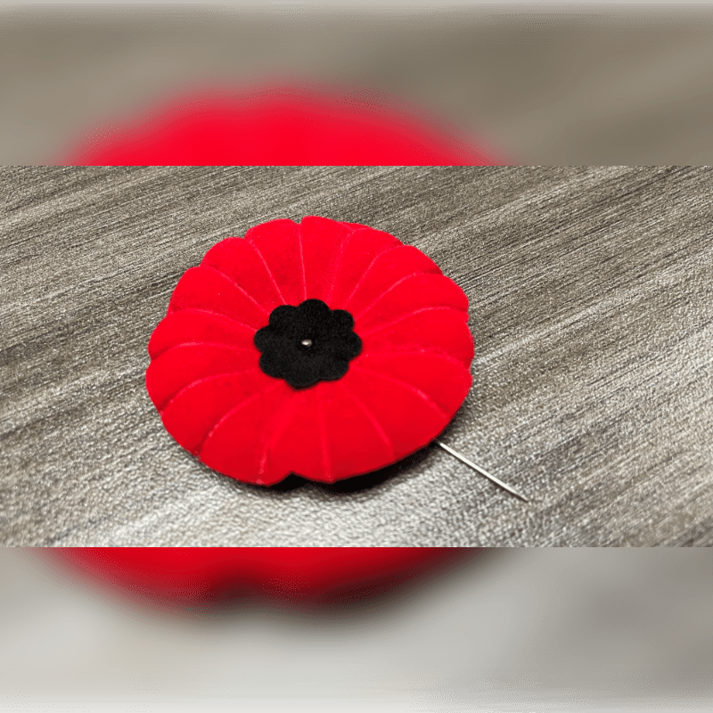 A red felt poppy with a black center sits on a grey textured surface.