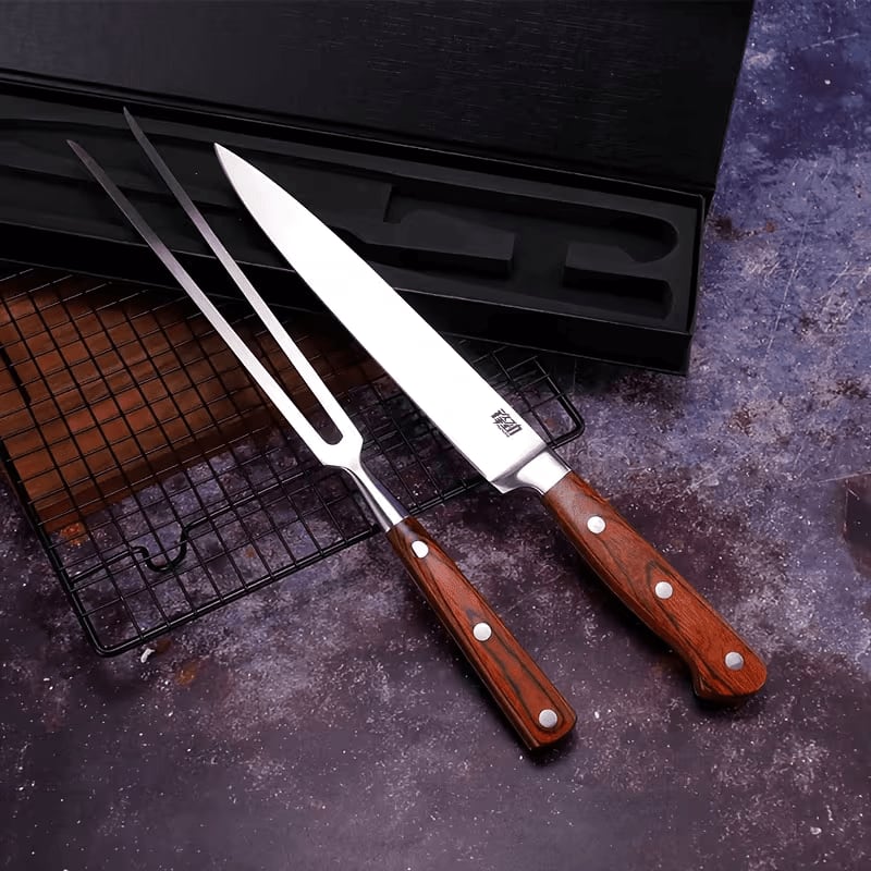 A carving knife and fork with wooden handles lie on a dark surface next to a wire rack and a black storage box.