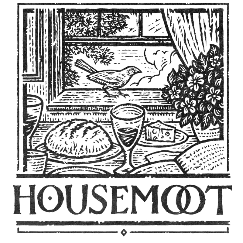 A table set with bread, cheese, and a glass of wine sits in the foreground, while a bird perches on a windowsill overlooking a garden in the background.