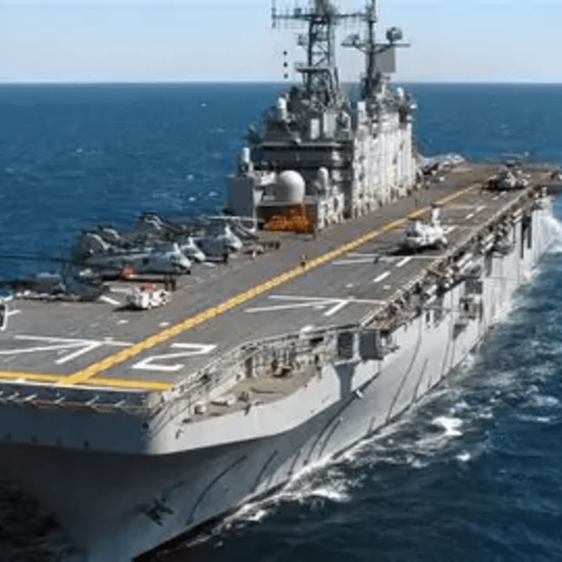 An aircraft carrier with jets on its deck sails through a vast blue ocean.