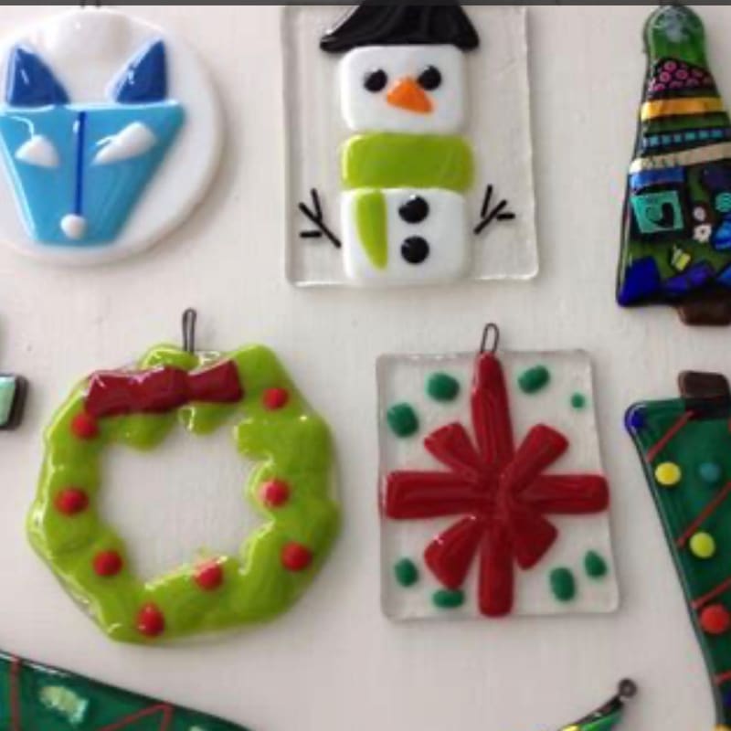 Colorful glass ornaments of a fox, snowman, wreath, and star are arranged against a plain white background.